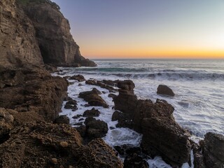 Coastal rocks at sunrise, waves crashing against the shore. Powerful ocean at dawn. Bethells Beach, Auckland, New Zealand