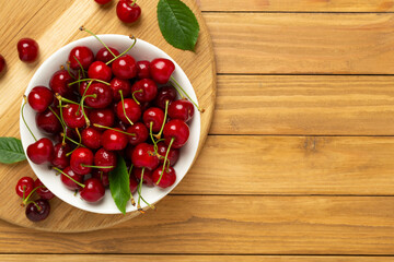 Fresh cherries in bowl on wooden background, top view