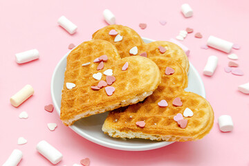 Belgian waffles heart shaped with sweet confetti,marsmallow.Valentines day dessert food,womens day, love,romance,pink background.