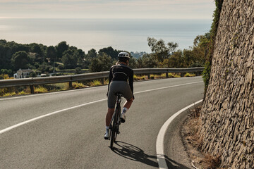 Fototapeta premium Cyclist rides along scenic coastal road. Enjoy the freedom of the open road and breathtaking views. Perfect for travel, sports, and active lifestyle imagery.
