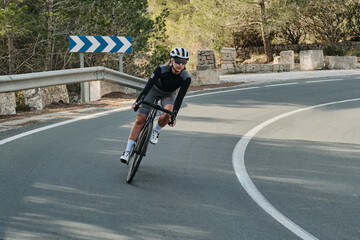 Female cyclist in grey cycling gear rides a road bike on a scenic winding road.  Sunlight casts shadows, creating a dynamic and active scene. Perfect for sports, fitness, and active lifestyle themes.