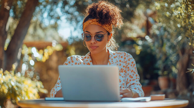 A focused freelancer working at a patio table with a laptop and notebook, set against a backdrop of trees and a bright, sunny day