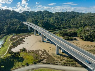 Obraz premium Aerial view of a highway bridge over a dried-up riverbed. Traffic flows smoothly across the modern concrete structure. Johnstones Hill Tunnels , Waiwera, Auckland, New Zealand