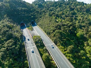 High-angle view of a highway cutting through lush New Zealand forest. Cars travel through tunnels,...