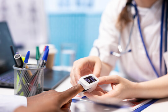 Medical specialist takes the oxygen saturation measurement and checking vital signs during a routine check up with her patient. Medic using an oximeter for accurate readings in office. Close up.