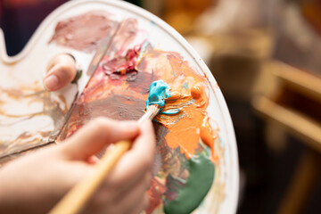 In an art studio, artist mixes a variety of watercolor paints on a palette to create a rustic masterpiece on canvas. Woman painting with tools and showing her skill, artwork creation. Close up.