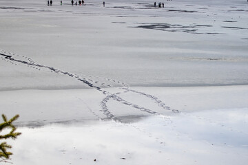 Footprints on Frozen Lake With Distant Figures Enjoying Winter Activities in a Serene Landscape