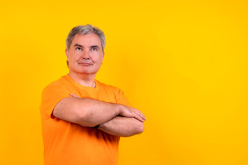Confident senior man crossing arms looking up on yellow background