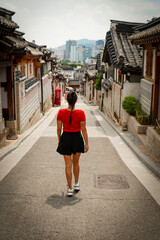 Woman Walking in a Traditional Korean architecture in a hanok village. Detailed wooden buildings with tiled roofs and stone walls. Captures the beauty and heritage of Korea.