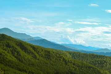 Panorama green forested hills and beautiful mountains under a cloudy blue sky