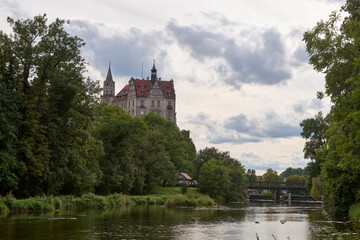 Obraz premium Picturesque Schloss Hohenzollern Castle Overlooking Tranquil River and Historic Bridge in Scenic German Countryside