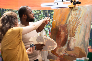 Team of artists painting a beautiful rustic creation on canvas, mixing colors together on a palette to create a nature inspired design. Diverse painters enjoy quality time in art studio.