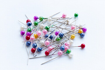A colorful array of sewing pins with rounded heads scattered on a white surface, showcasing various vibrant hues ideal for crafting and sewing.