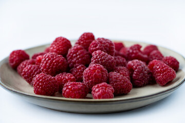A plate filled with fresh, plump raspberries showcases their vibrant red hue and juicy texture, perfect for snacking or adding to desserts.