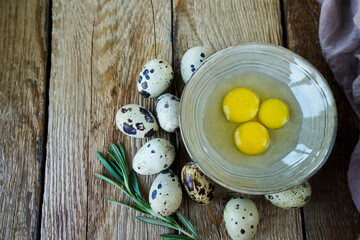 A rustic scene featuring a bowl with three bright egg yolks surrounded by quail eggs on a wooden surface, accented with green rosemary.