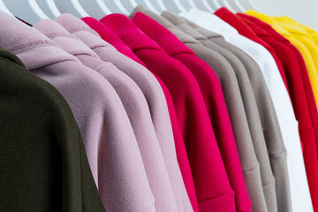 A vibrant array of hoodies hanging on hangers, showcasing a variety of colors including pink, red, gray, white, and yellow, highlighting modern fashion choices.