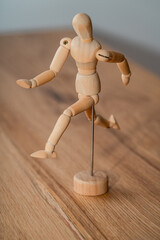A wooden artist mannequin strikes a dynamic pose on a wooden surface, showcasing its adjustable limbs for drawing and sculpting inspiration.