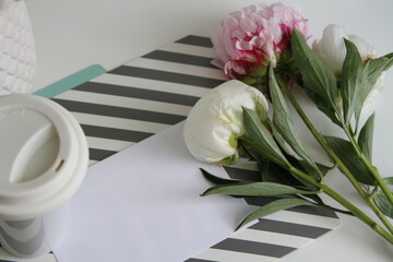 Fresh peonies, cup of coffee and white sheet of paper on the table