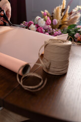 Florist makes a composition of flowers from roses and carnations for the client. Wrapping a bouquet from mixed flowers in pack paper by florist in floral shop.