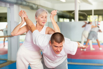 Senior woman exercising elbow strike on man during self-protection training.