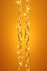 Shimmering golden chains illuminated with sparkling effects against a warm orange background