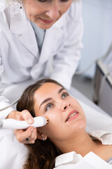 Mature female dermatologist performing cosmetology procedure for young woman, RF lifting and vacuum massage for facial skin therapy in clinic