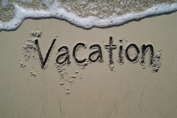 The word vacation written in the sand in a tropical setting