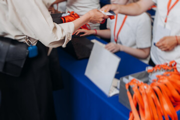 Process of checking in on conference congress forum event, registration desk table, visitors and attendees receiving lanyard with name badge and entry wristband bracelet and register electronic ticket