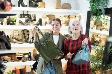 Elderly woman with young girl friend inspects shop window and is looking for modern, fashionable and roomy shoulder bag. In leather goods store, customers make choice of product with reasonable price