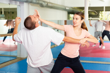 Caucasian woman performing chin strike while sparring with man in gym during self-defence training.