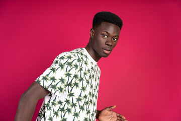 Young black man wearing t-shirt with palm tree print posing on pink background