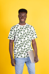 Smiling young man holding laptop on yellow background