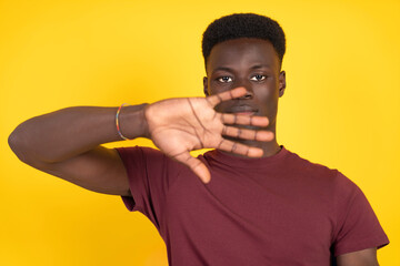 Young man covering face with hand on yellow background