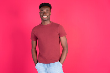 Young black man smiling with hands in pockets on pink background