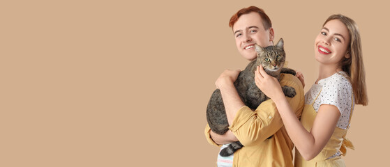 Young couple with cute cat on beige background