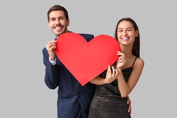 Beautiful young couple with red paper heart on grey background. Valentine's day celebration