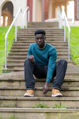 Fototapeta premium Young man sitting on stairs in front of university building