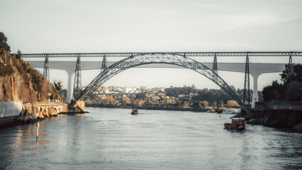 Obraz premium Iconic&nbsp;telephoto view of Porto, Portugal, featuring the Dona Maria Pia Bridge and Sao Joao Bridge spanning the Douro River, with scenic hillsides and boats on calm waters