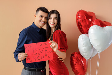 Young engaged couple with wedding ring and sign I LOVE YOU on beige background. Valentine's Day celebration