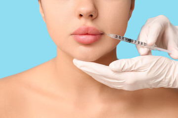 Young woman receiving filler injection in lips on blue background, closeup