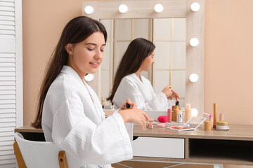 Beautiful young woman doing makeup at dressing table at home