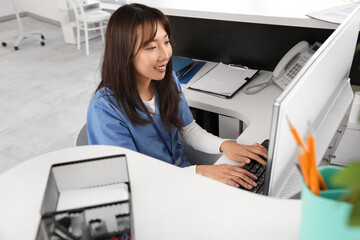 Female Asian medical intern working with computer at reception in clinic
