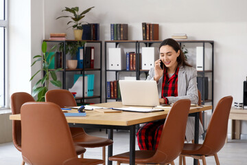 Young businesswoman talking by mobile phone at table in office. National Wear Your Pajamas to Work Day