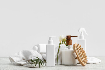 Set of cosmetic products, massage brush, clean towel and flower on light table