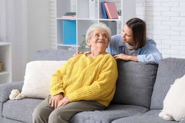 Young nurse and senior woman sitting on sofa at home