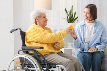 Senior woman in wheelchair taking pills from nurse at home