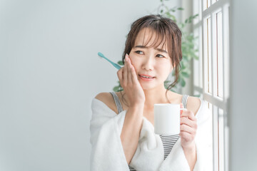 虫歯が痛い・しみて頬を押さえるアジア人女性
