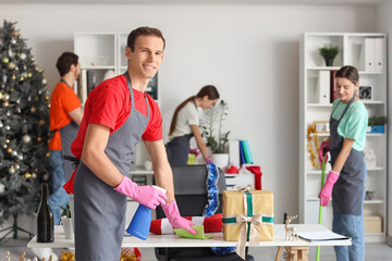 Male janitor cleaning table and his team in office after New Year party