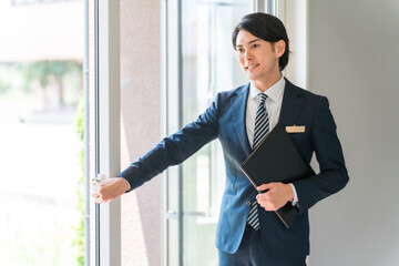 窓・ドア・サッシ・ガラス戸・鍵を案内するビジネスマン（樹脂サッシ・省エネ基準）
