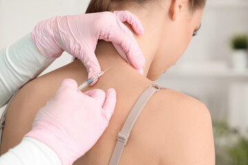 Young woman receiving injection at cosmetologist's office, back view